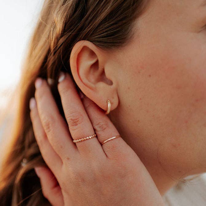 Close-up of a person wearing gold hoop earrings and rings.