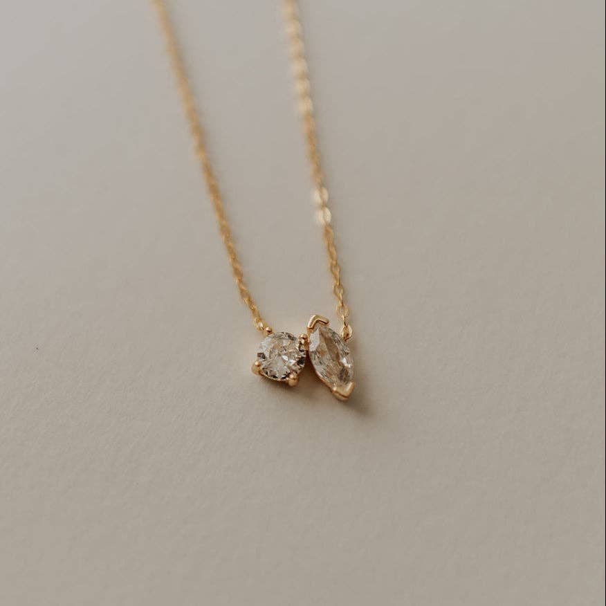 Gold necklace with two diamond pendants on a neutral background