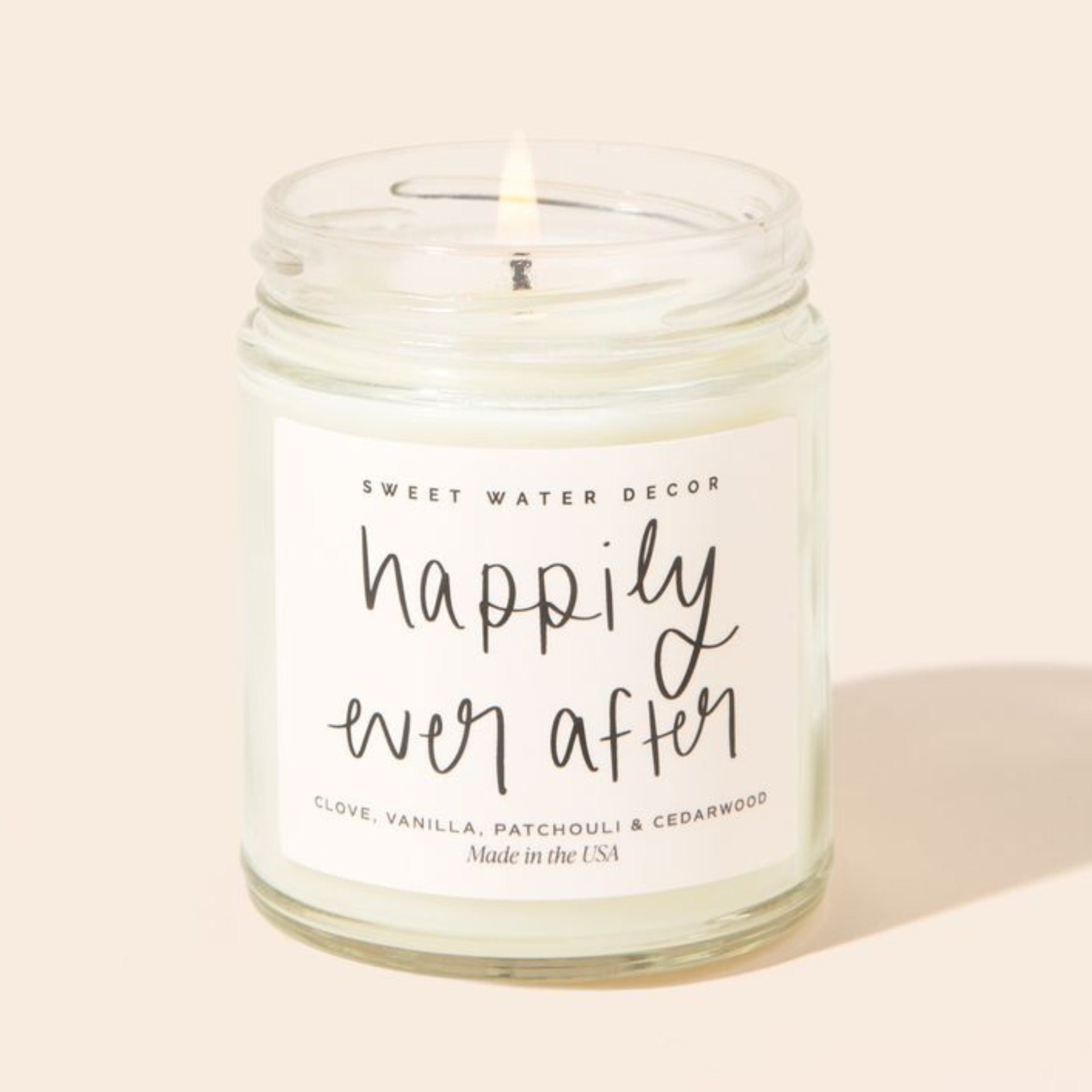 Candle in a glass jar with a label reading 'happily ever after' on a beige background