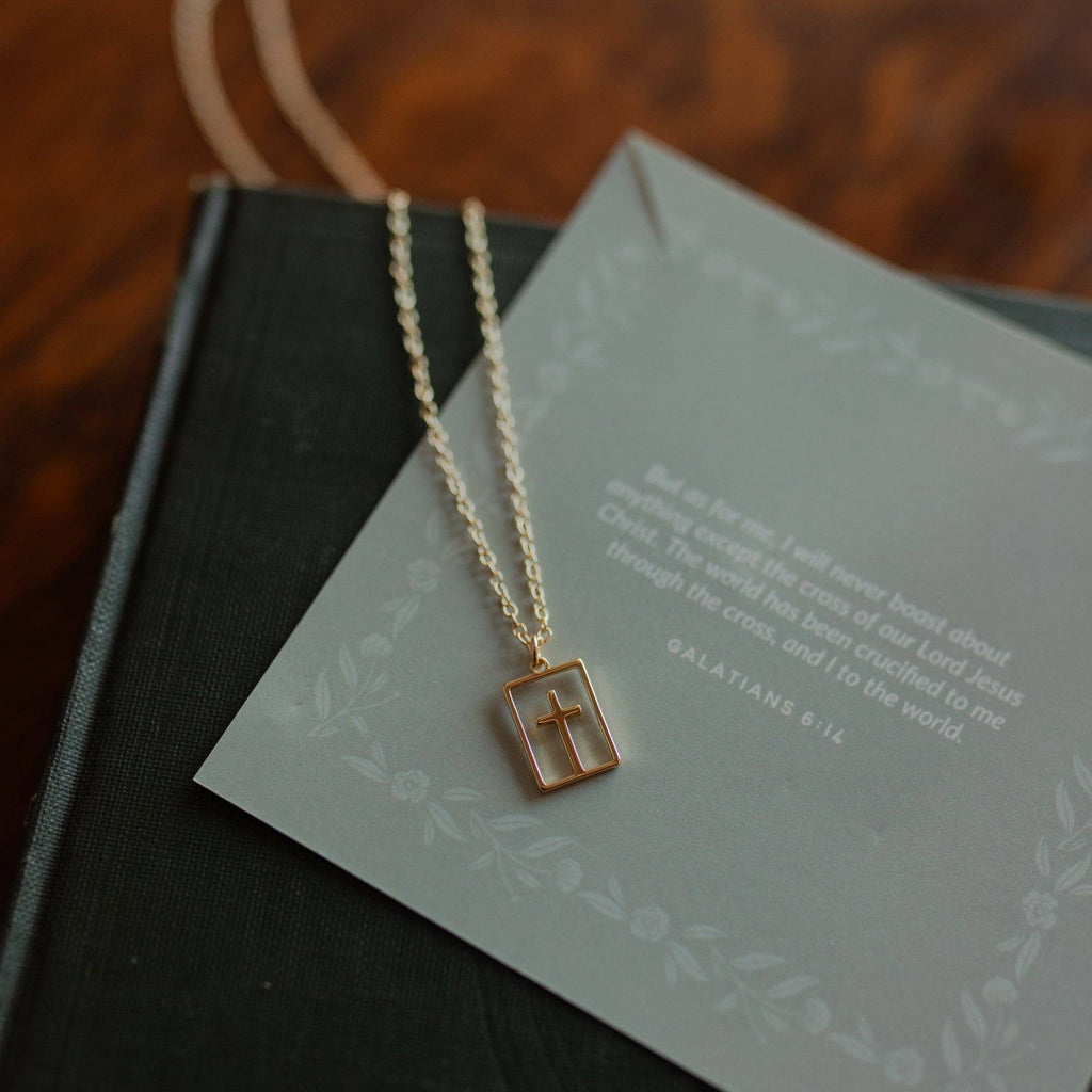 Gold necklace with a cross pendant on a green card with text
