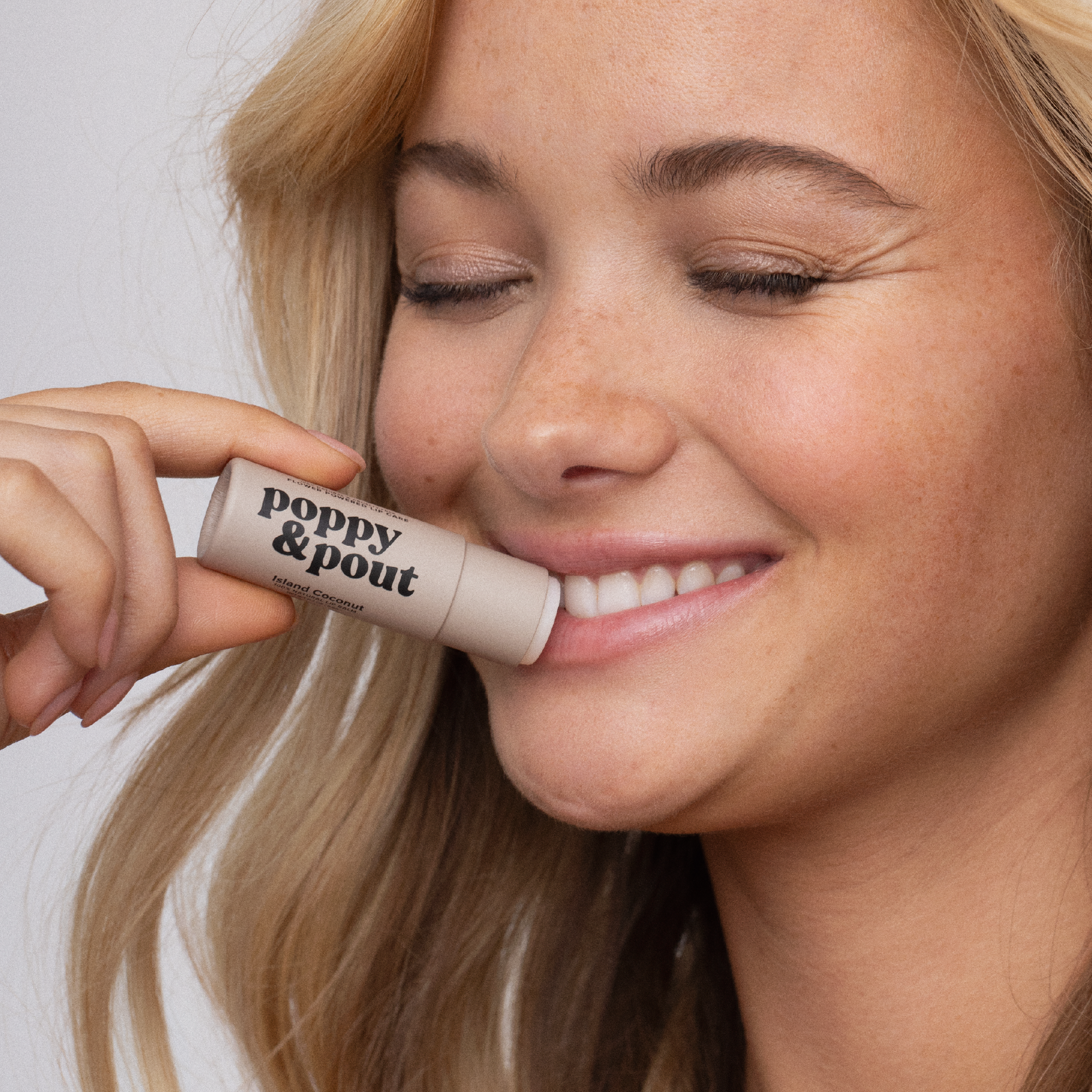 Woman holding a 'poppy & pout' lip balm close to her lips.
