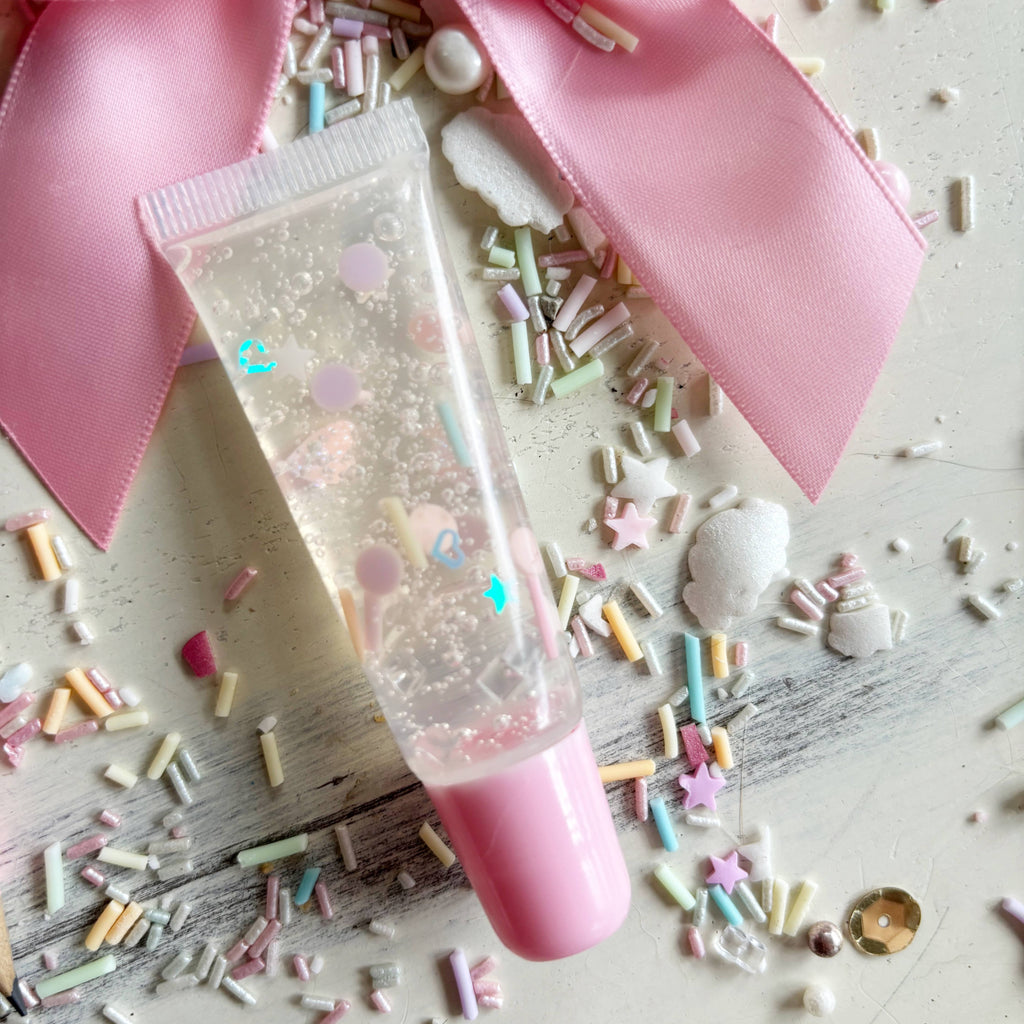 Clear tube with pink cap surrounded by colorful sprinkles on a light wooden surface