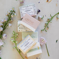 Collection of natural soap bars with floral packaging on a light surface with flowers and leaves.