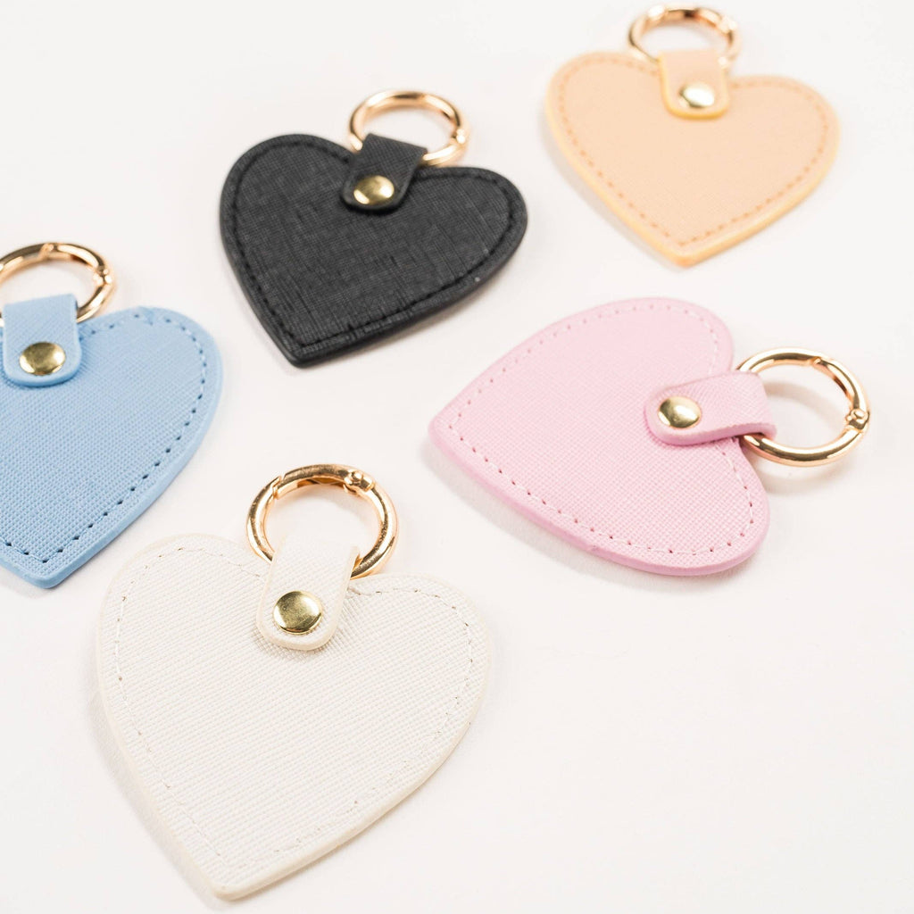 Violet & Brooks J’adore heart bag charms in blush pink, blue, black, cream, and pale yellow with gold-tone clasps.
