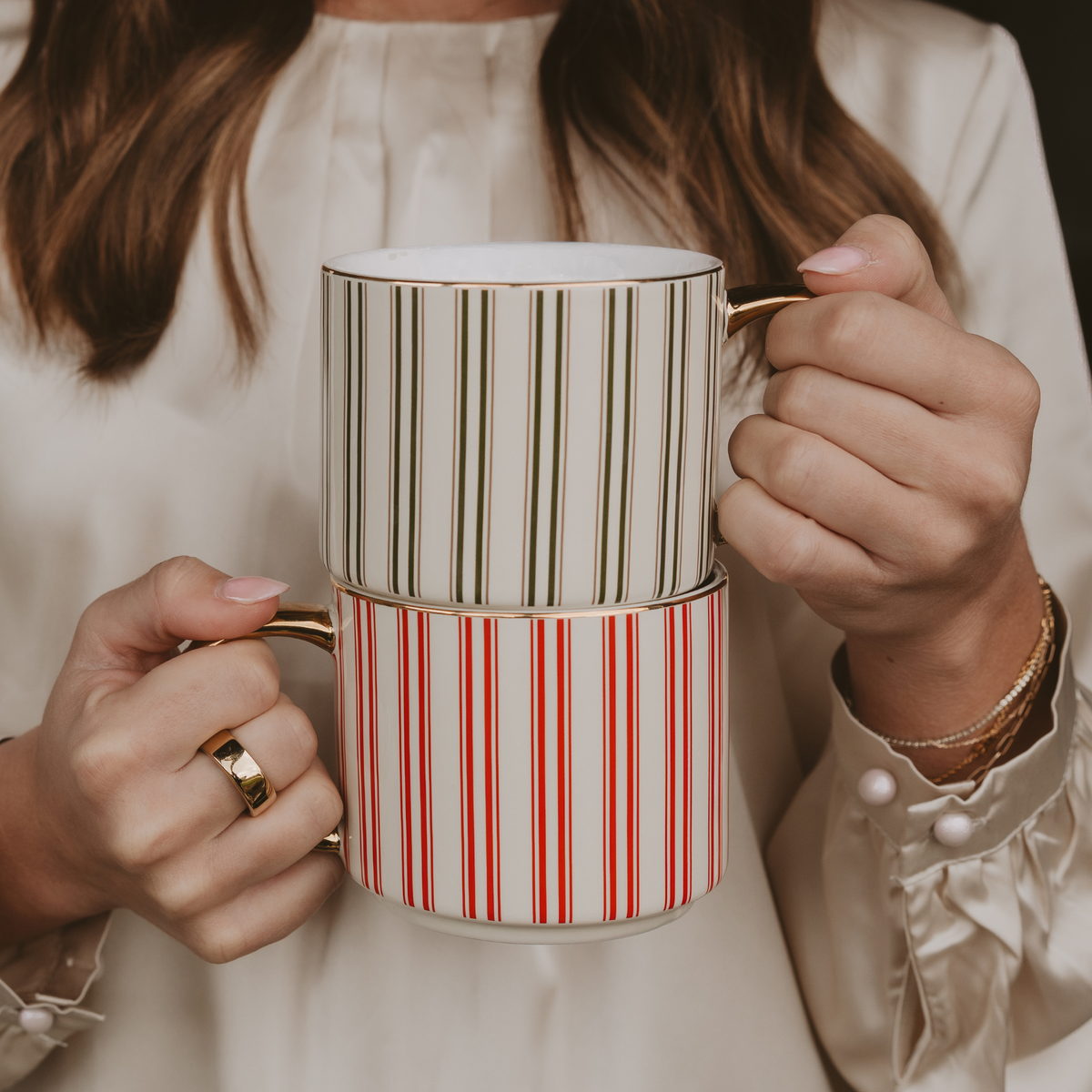 Person holding a green striped mug stacked on a red striped mug, both with gold handles.
