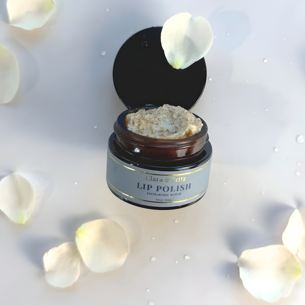 Open jar of lip polish with white petals on a light background