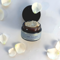 Open jar of lip polish with white petals on a light background