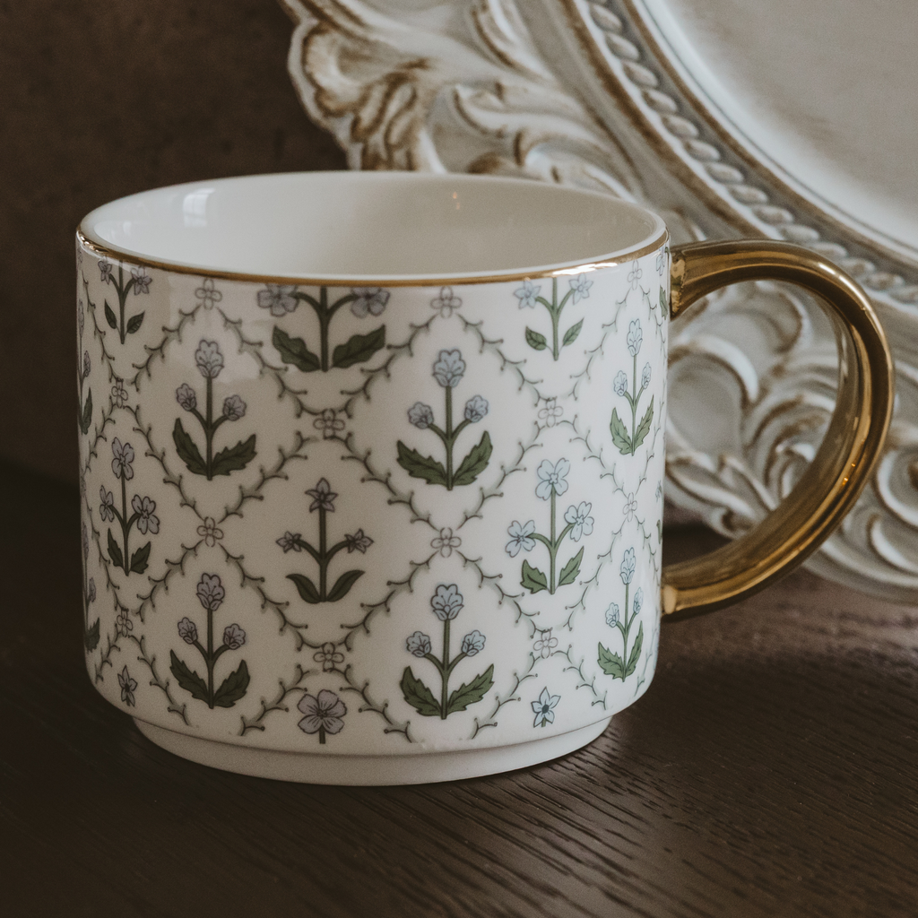 White mug with floral pattern and gold handle on a wooden surface