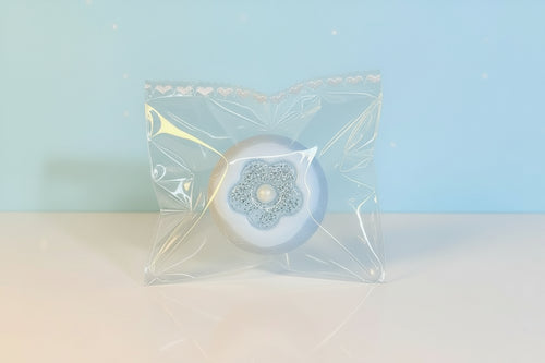 Blue Persimmon TABA Squishy with floral center in clear packaging against a soft blue background.