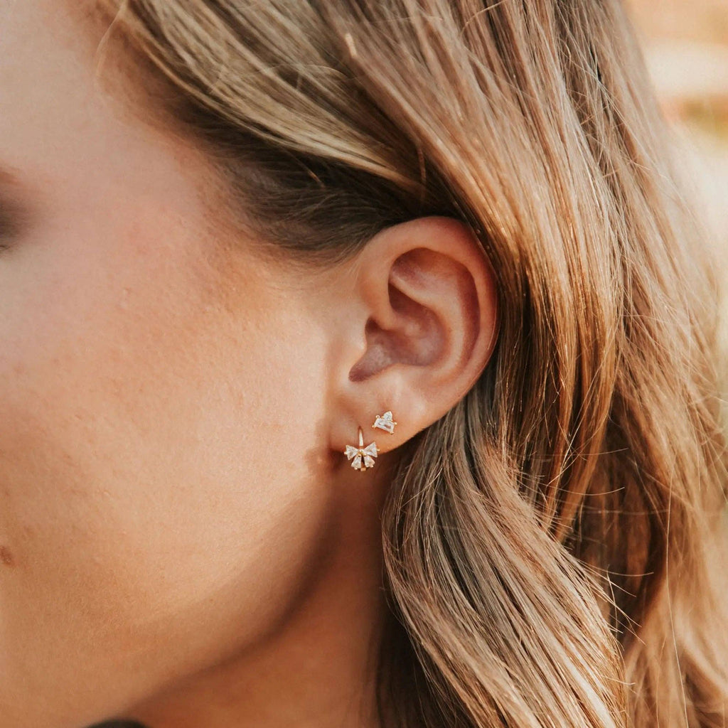 Close-up of a person wearing a bow-shaped earring with a blurred background