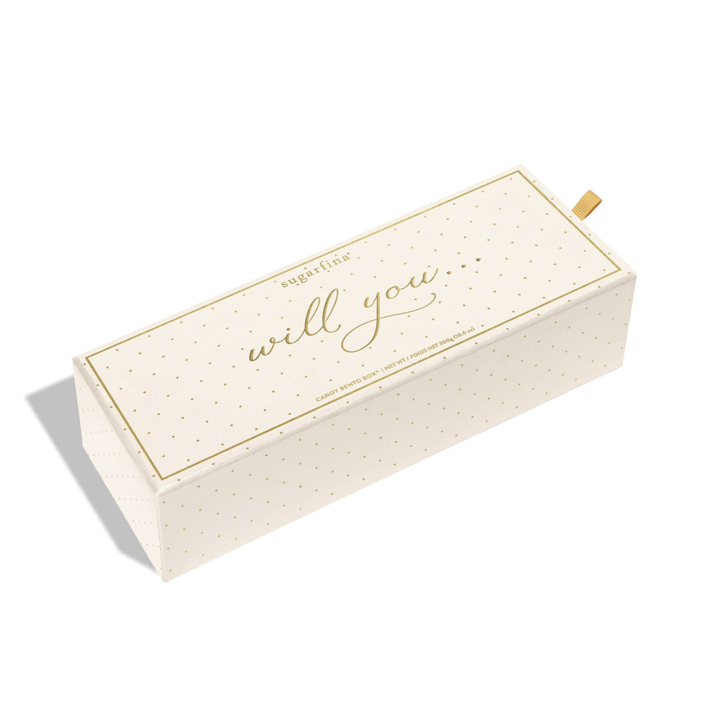 A cream-colored rectangular gift box with gold polka dots and the words 'will you.