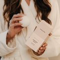Person holding a white candle and a pink book titled 'Waldorf's Animal' in a cozy setting.
