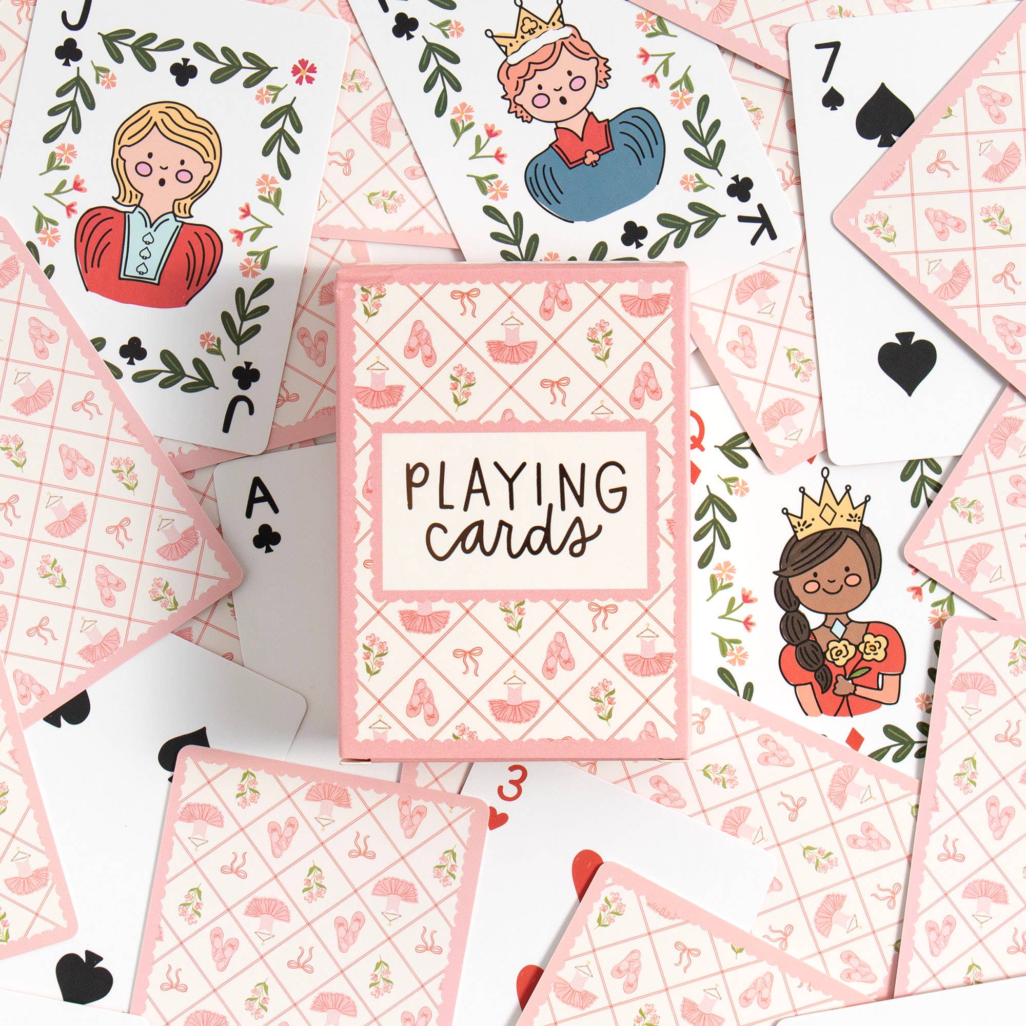 A flat-lay of a pink and white playing card deck box labeled 'PLAYING cards' surrounded by illustrated playing cards on a white background.