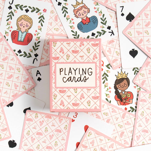 A flat-lay of a pink and white playing card deck box labeled 'PLAYING cards' surrounded by illustrated playing cards on a white background.