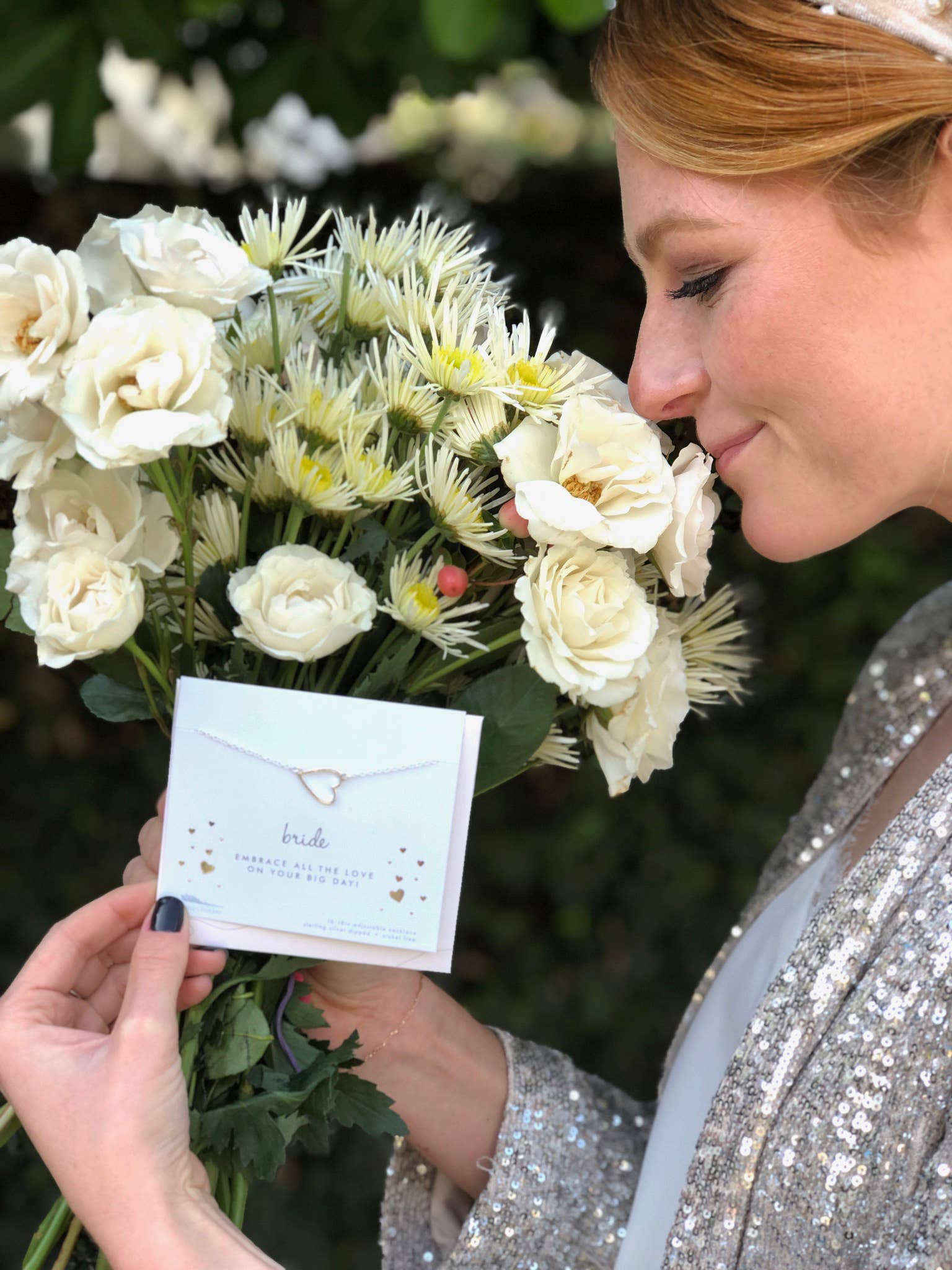 Woman holding a bouquet of white flowers and a card with a necklace design.