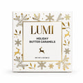 Lumi Holiday Butter Caramels packaging box, featuring a white background with elegant gold foil snowflakes, leaves, reindeer, and a central gold-bordered label with black text.