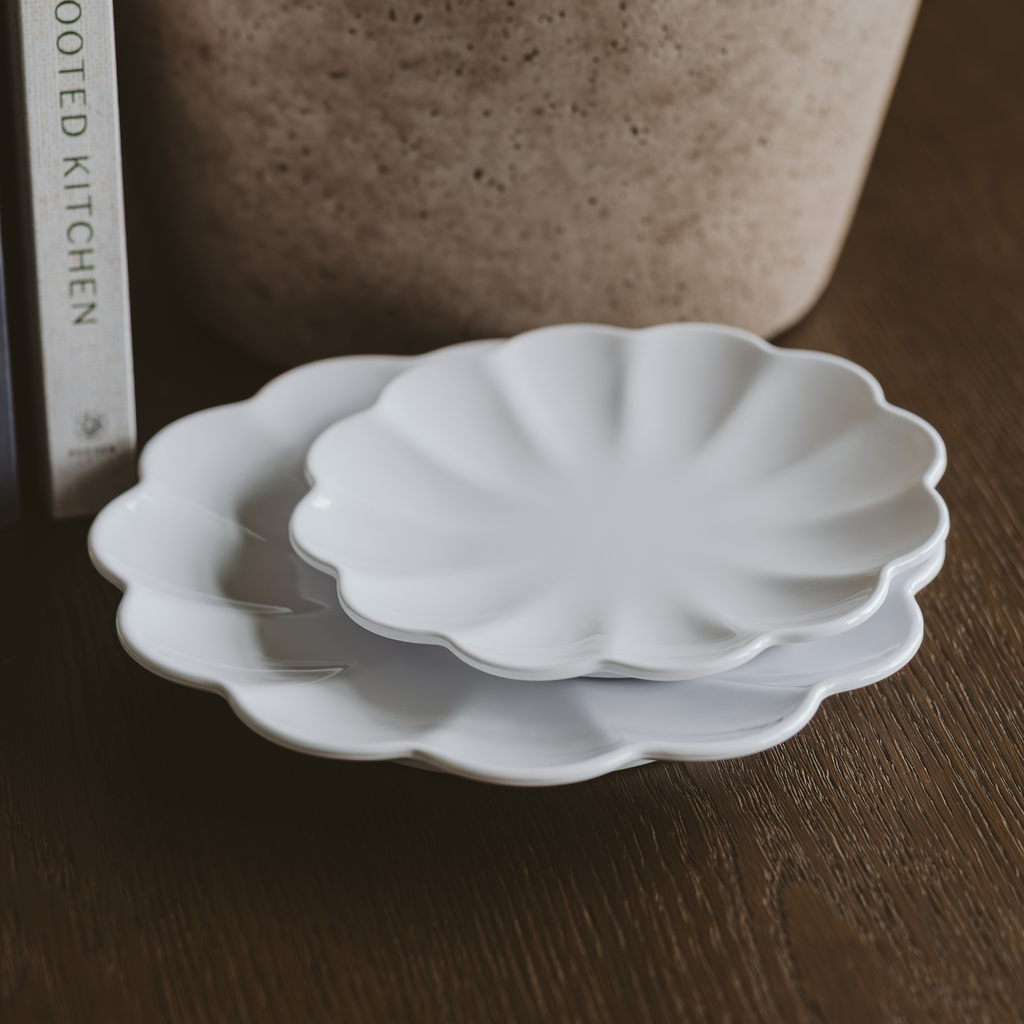 Two white ceramic plates with scalloped edges stacked on a wooden surface.