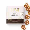 LUMI Classic Mini Pretzels 2 oz cream and brown box with gold lettering beside salted mini pretzels on a white background.
