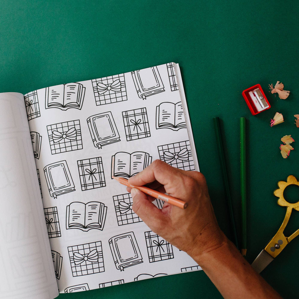 Hand holding a pen over a coloring book with black line art on a green background