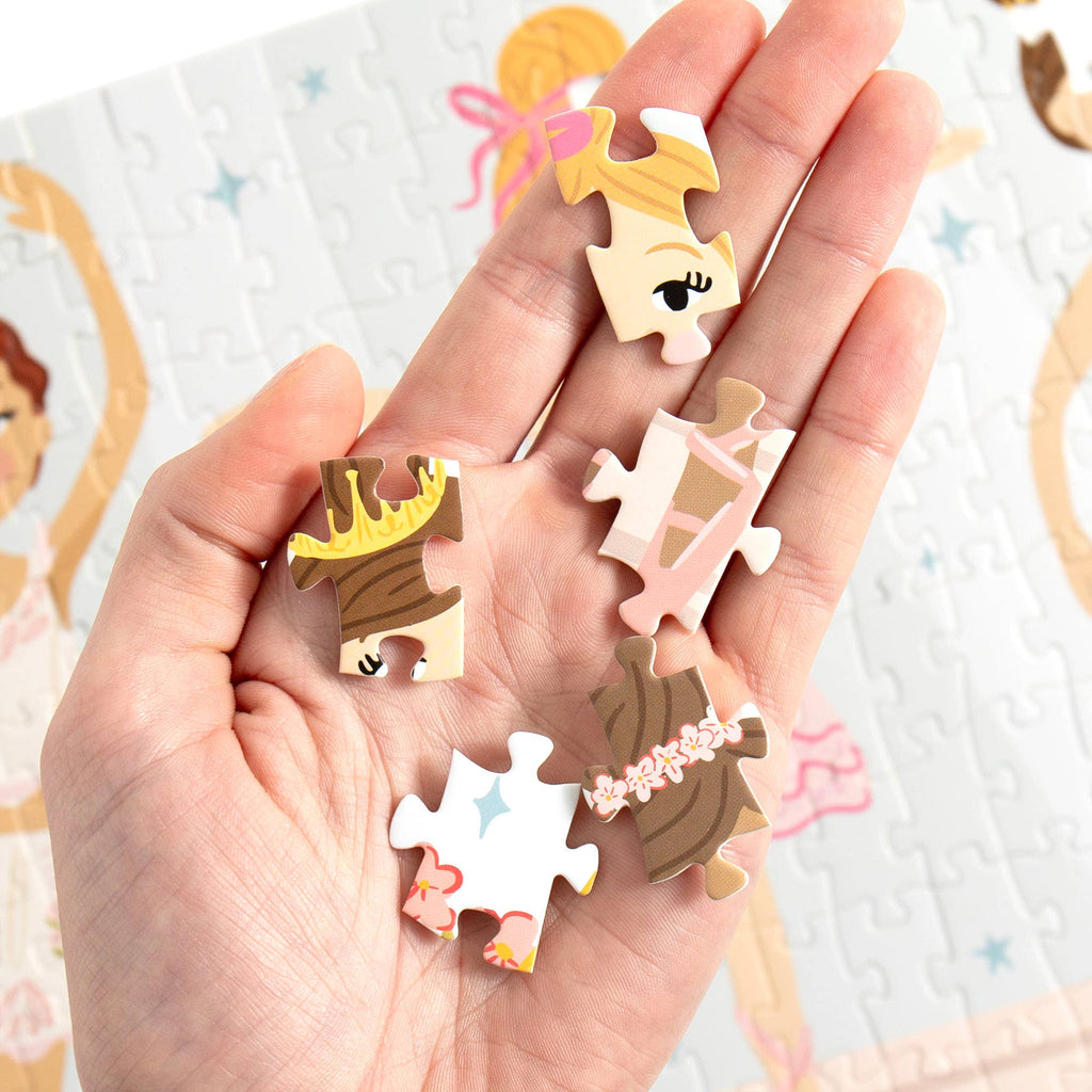 A hand holds several small, illustrated jigsaw puzzle-piece charms with cartoon character faces and hair details, set against a soft-focus background of a completed puzzle.