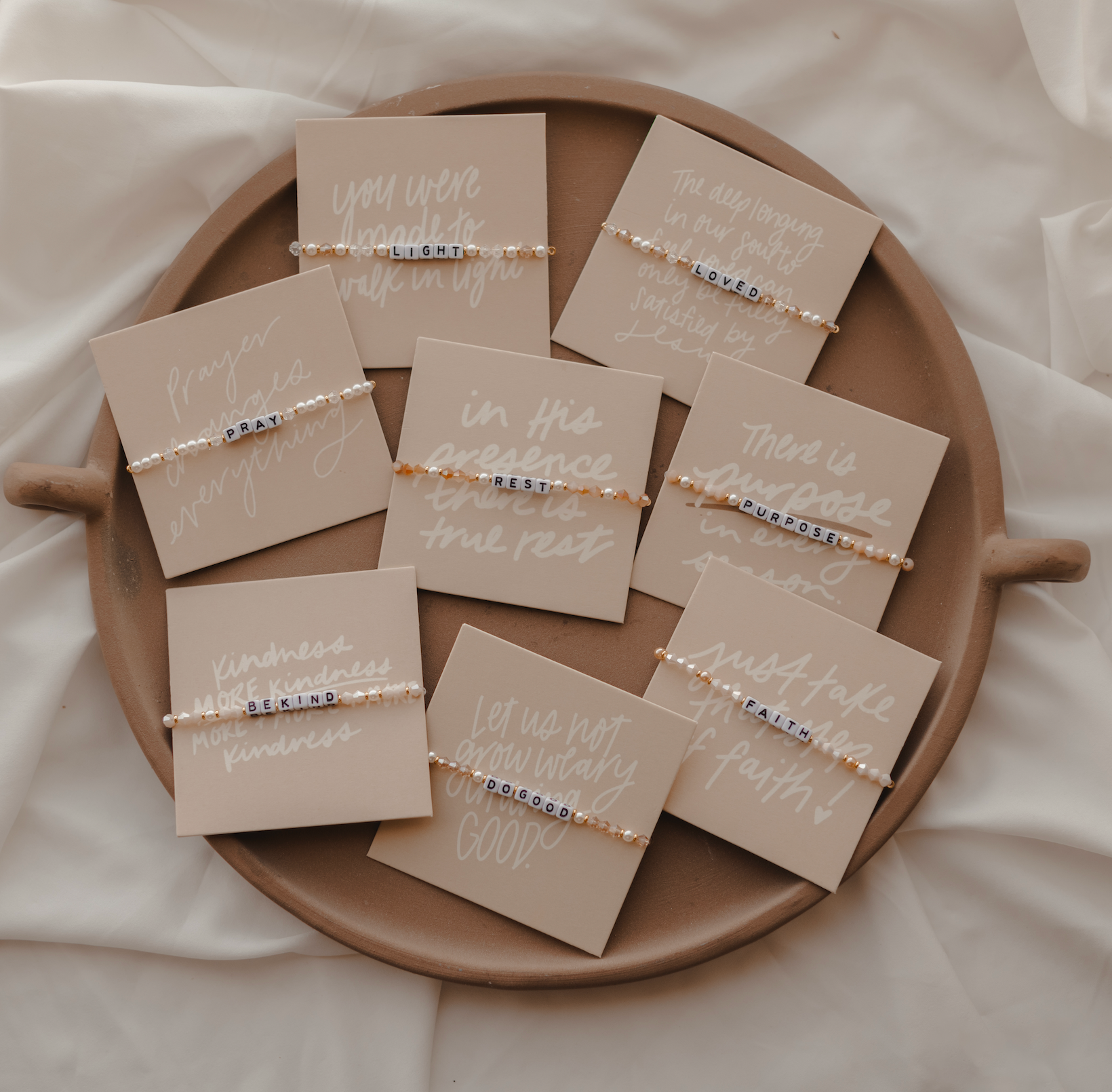 Bracelets with inspirational messages on cards displayed on a wooden tray.