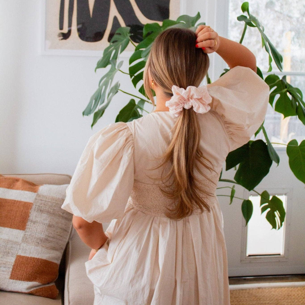 Woman in a white dress with a floral hair accessory standing in a bright living room.