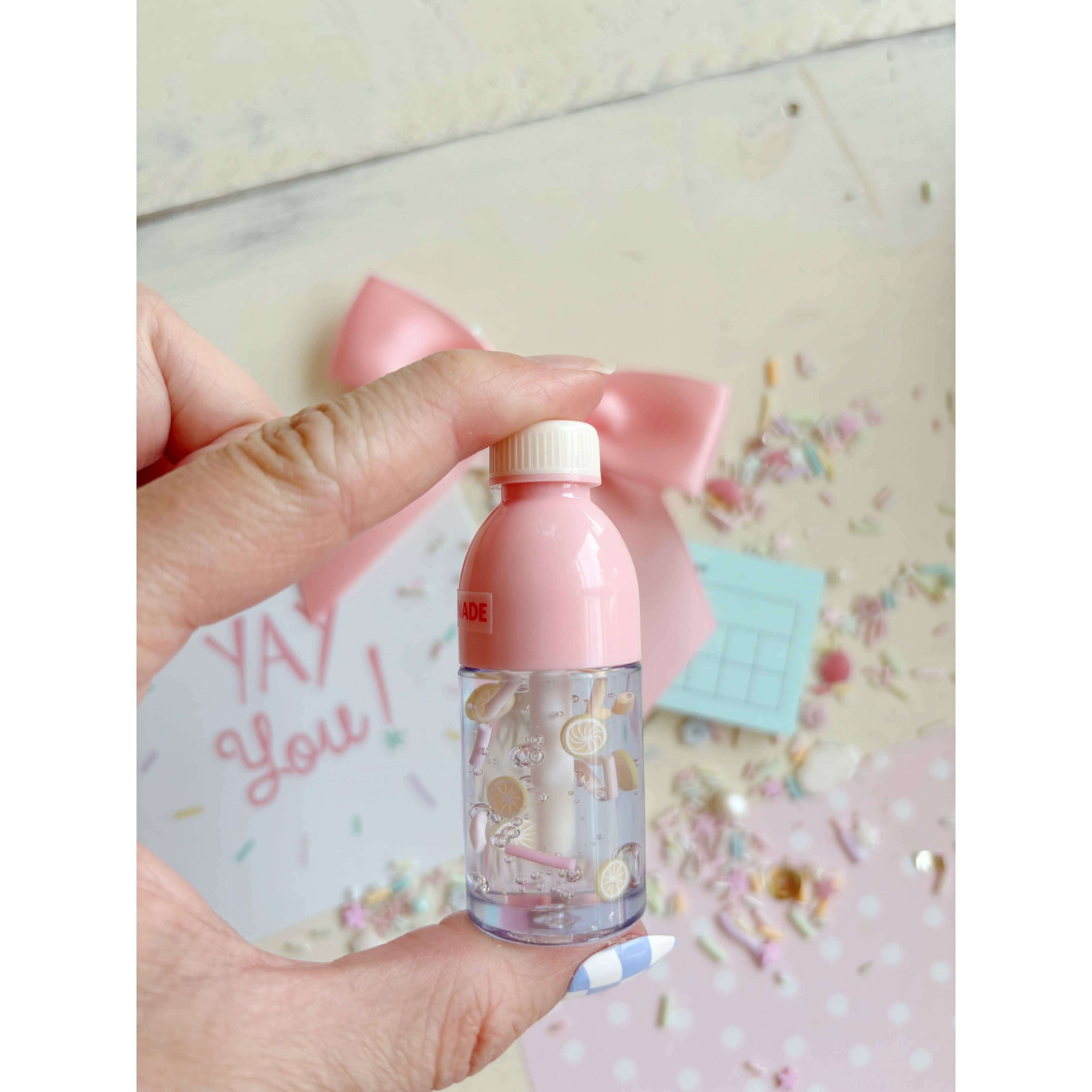 Small bottle with a pink cap held by a hand, with a decorative background.
