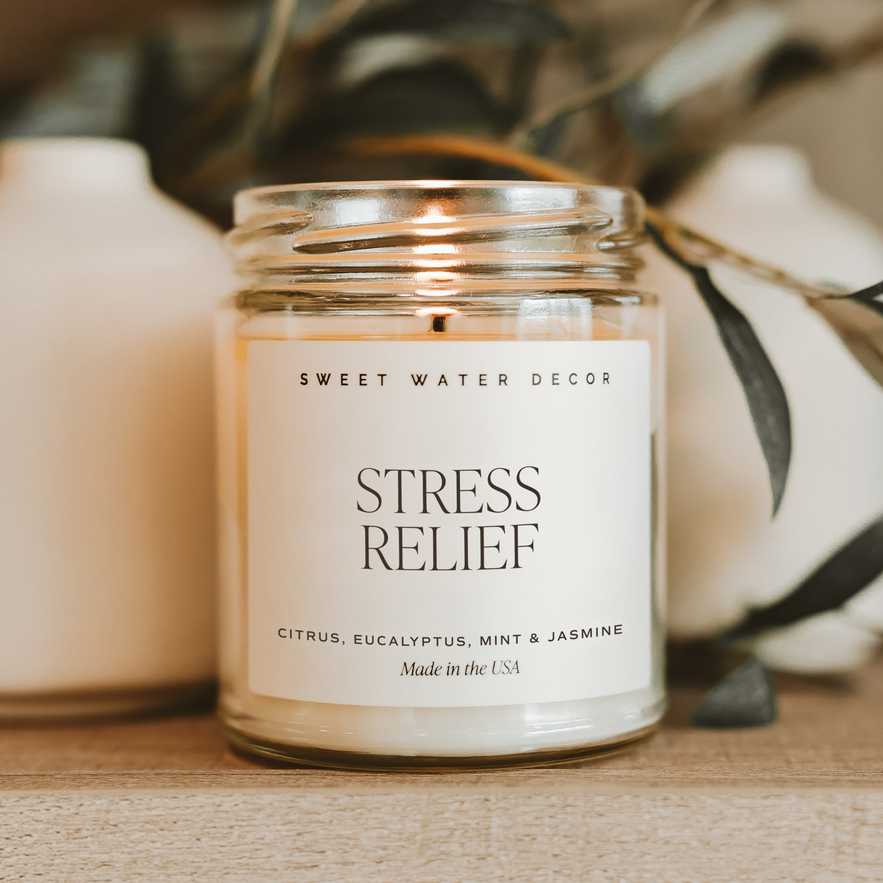 Candle labeled 'Stress Relief' by Sweet Water Decor on a wooden surface with decorative elements.