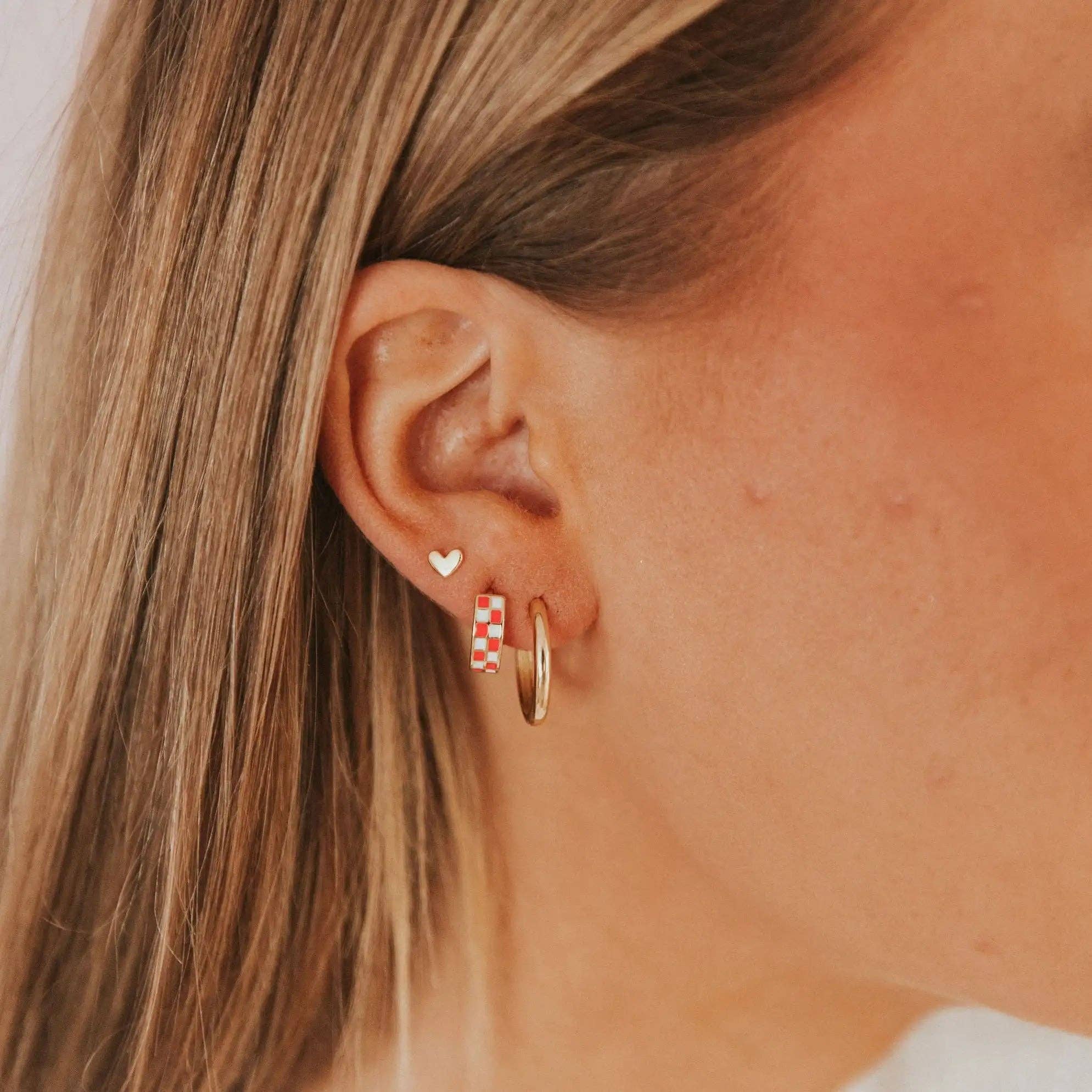Close-up of an ear wearing a gold hoop earring and a small heart-shaped earring.