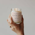 Hand holding a candle jar with 'you're the best!' text on a neutral background