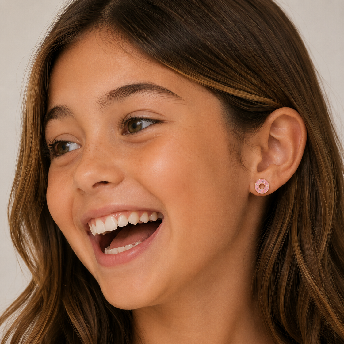 Close-up of a young girl with a bright smile wearing pink earrings.