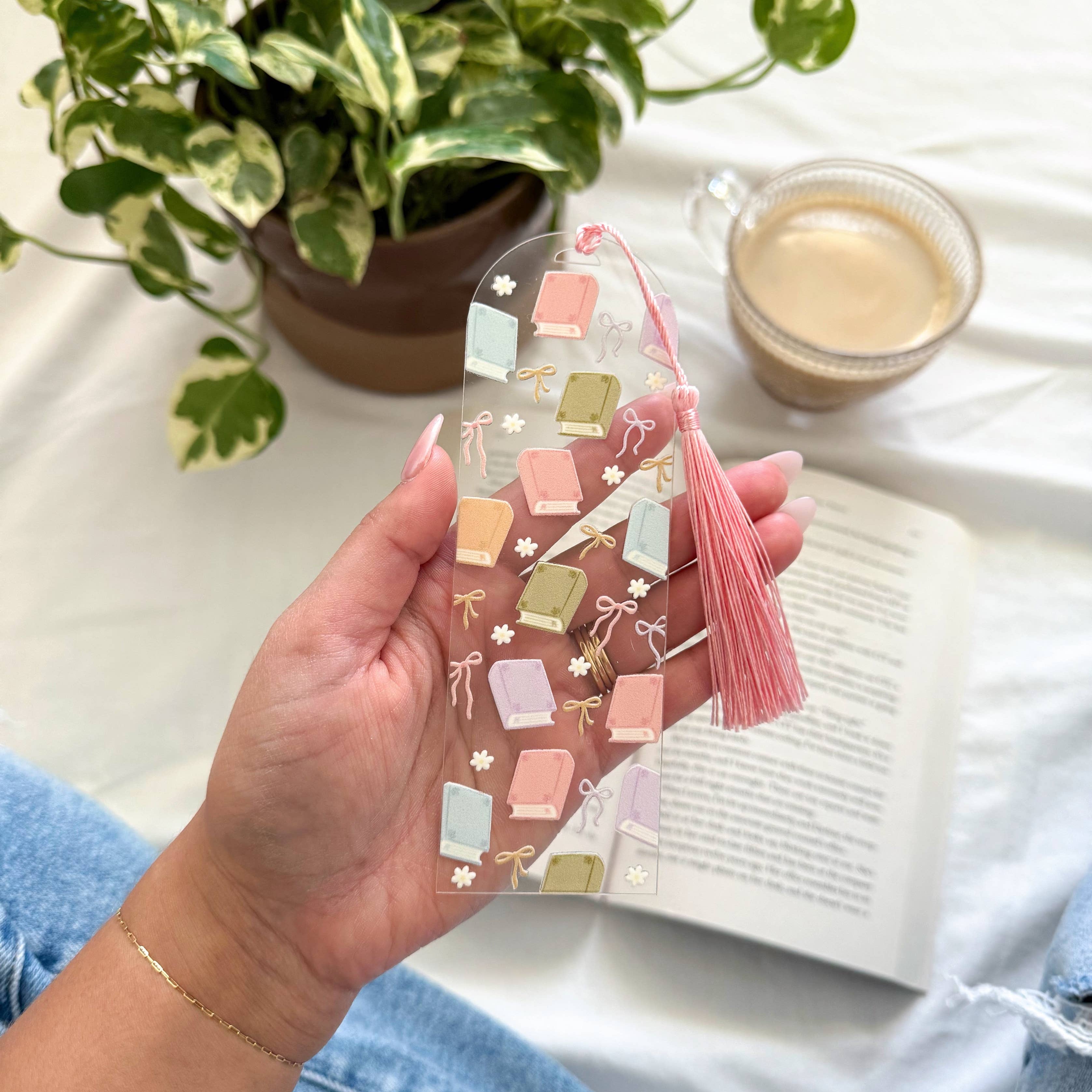 Hand holding a clear phone case with decorative elements on a white surface with a plant and cup of coffee.