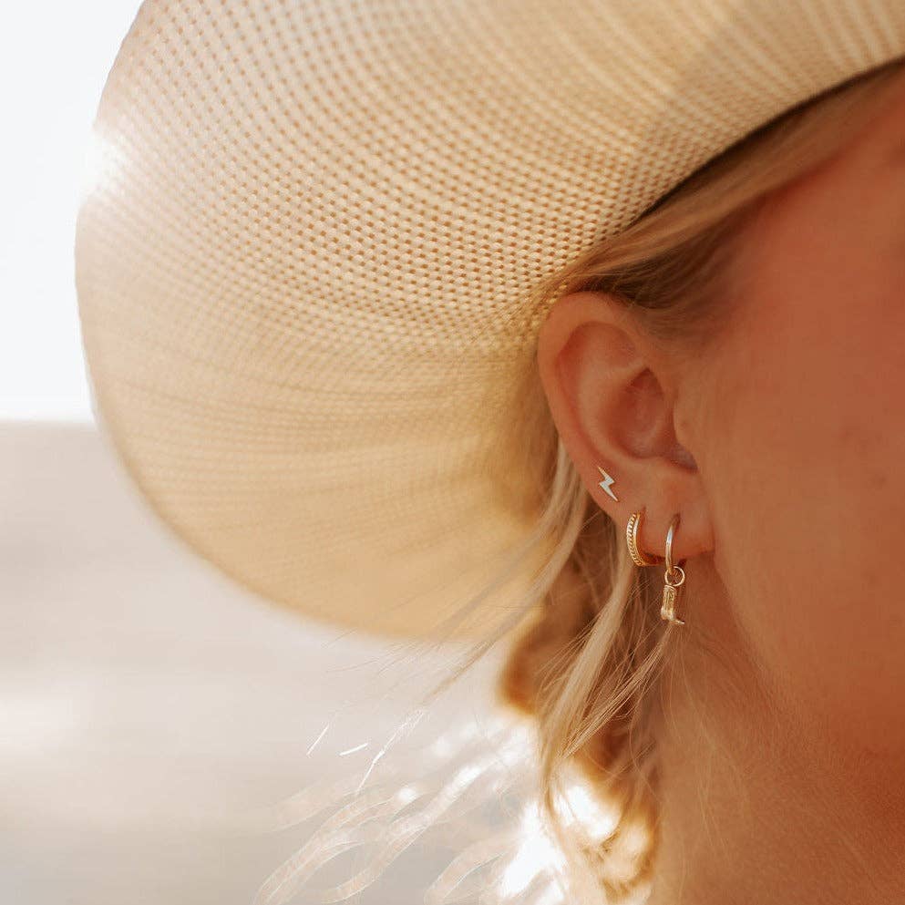 Close-up of a person wearing gold hoop earrings with a straw hat and white top.