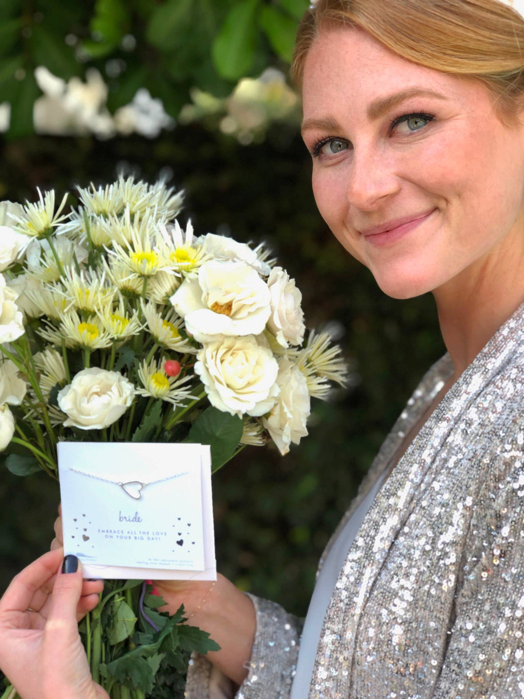 Woman holding a bouquet of white flowers and a card with a necklace design.