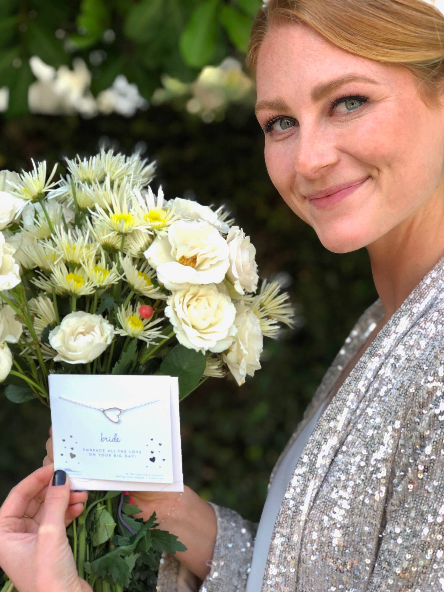 Woman holding a bouquet of white flowers and a card with a necklace design.