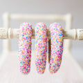 Three colorful sprinkle-dusted hoop earrings on a white stand.