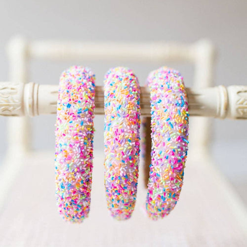 Three colorful sprinkle-dusted hoop earrings on a white stand.