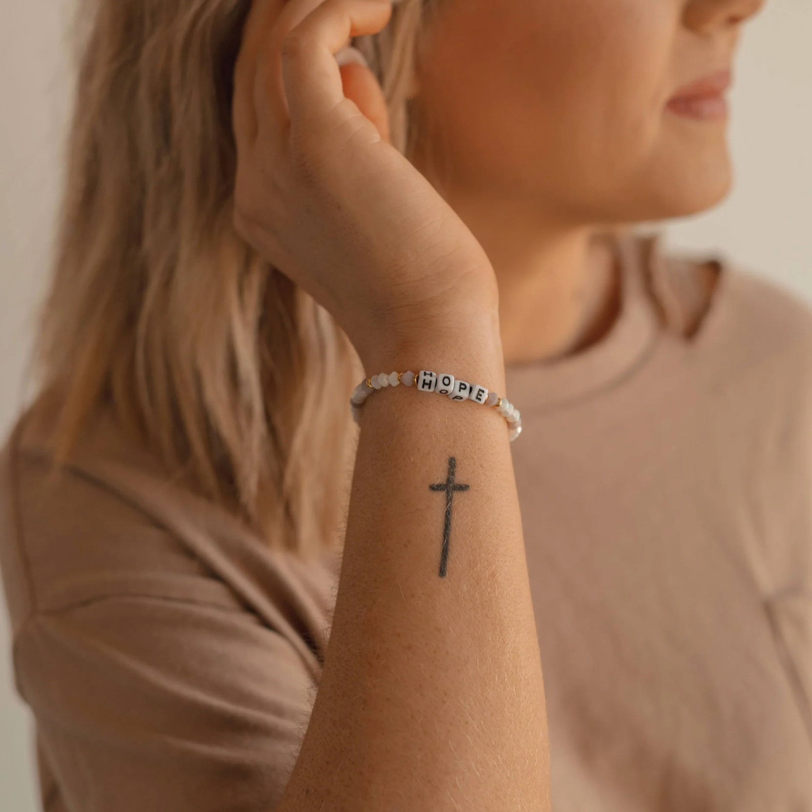 Person wearing a bracelet with 'hope' on their wrist, with a neutral background