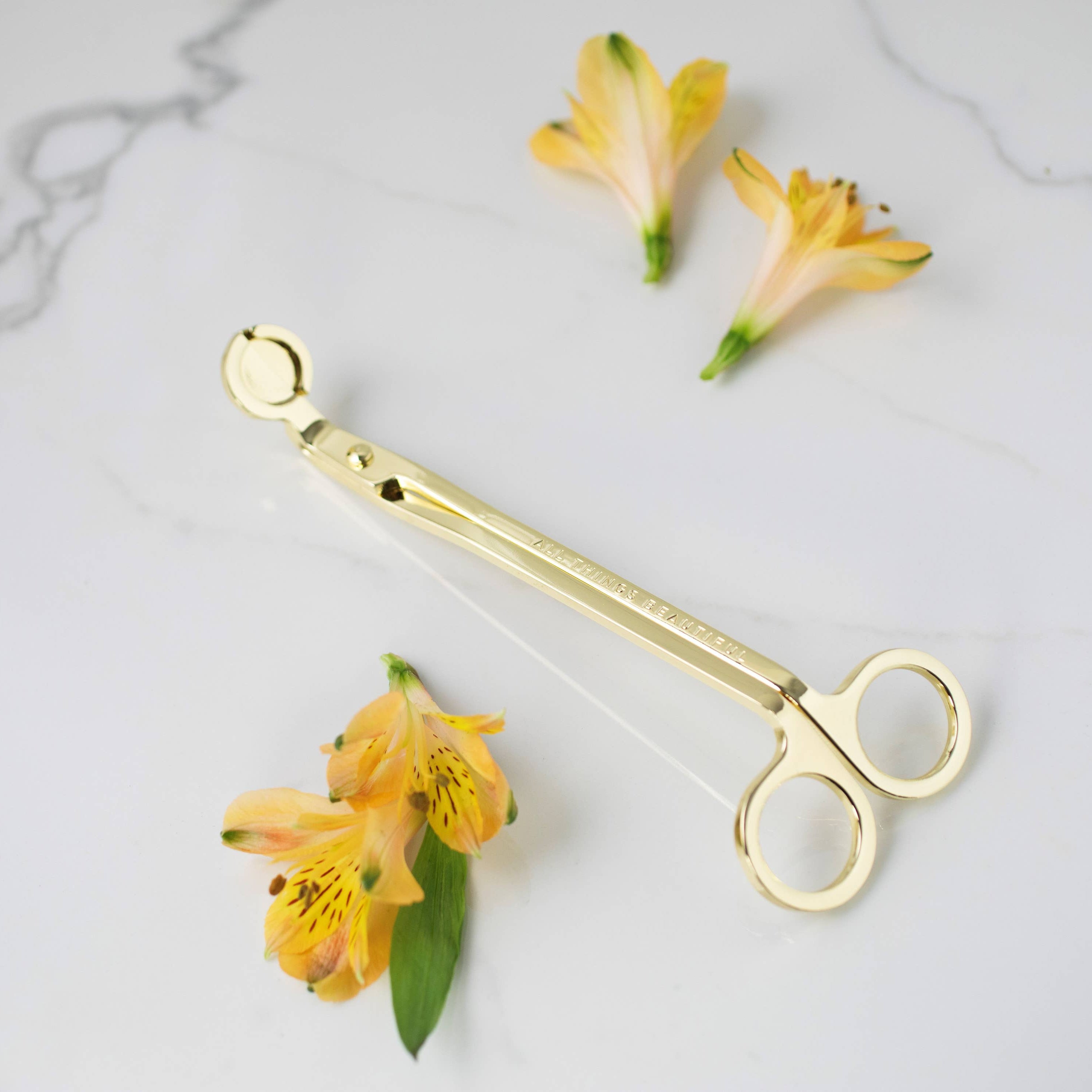 Gold scissors on a marble surface with yellow flowers
