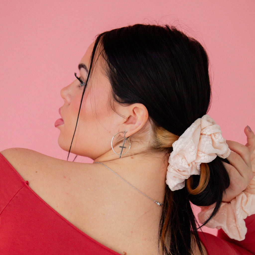 Woman with a ponytail wearing a pink scrunchie against a pink background
