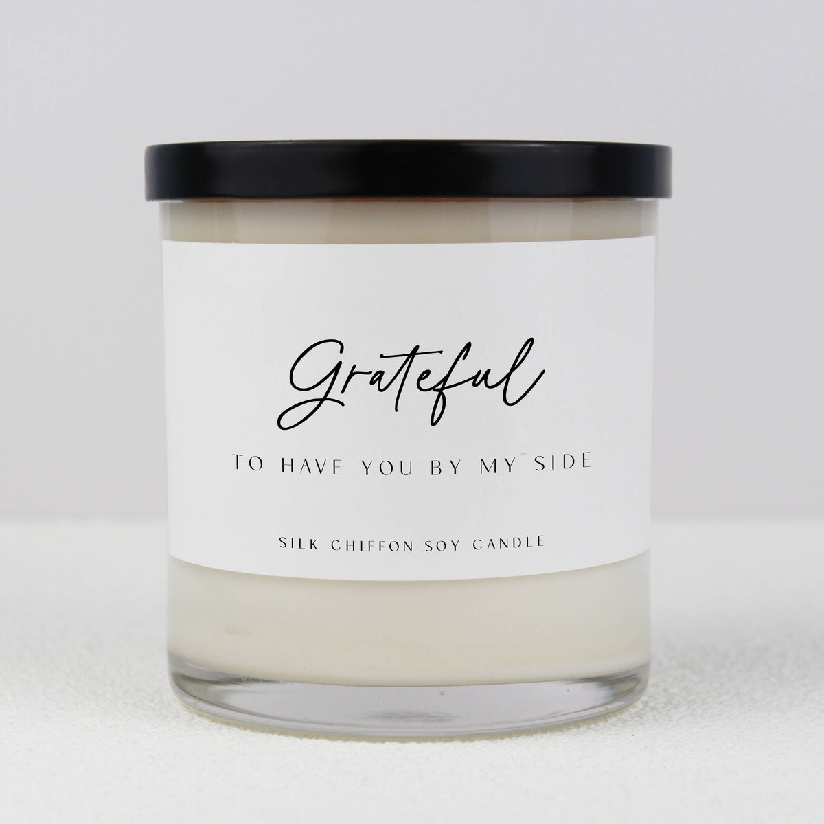 Mother of the Bride Definition Soy Candle in a white glass jar with a sentimental label, displayed on a clear pedestal against a soft pink background.