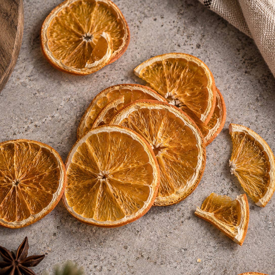 loose slices close-up: Whole and broken dried orange slices scattered on a gray surface beside star anise and a linen cloth.