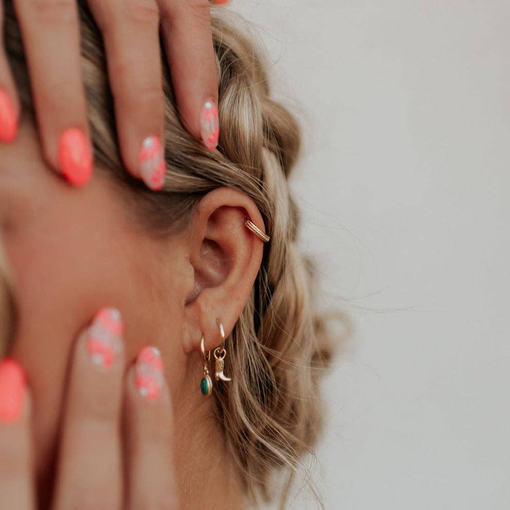 Close-up of an ear with gold earrings and a hand adjusting hair, on a neutral background
