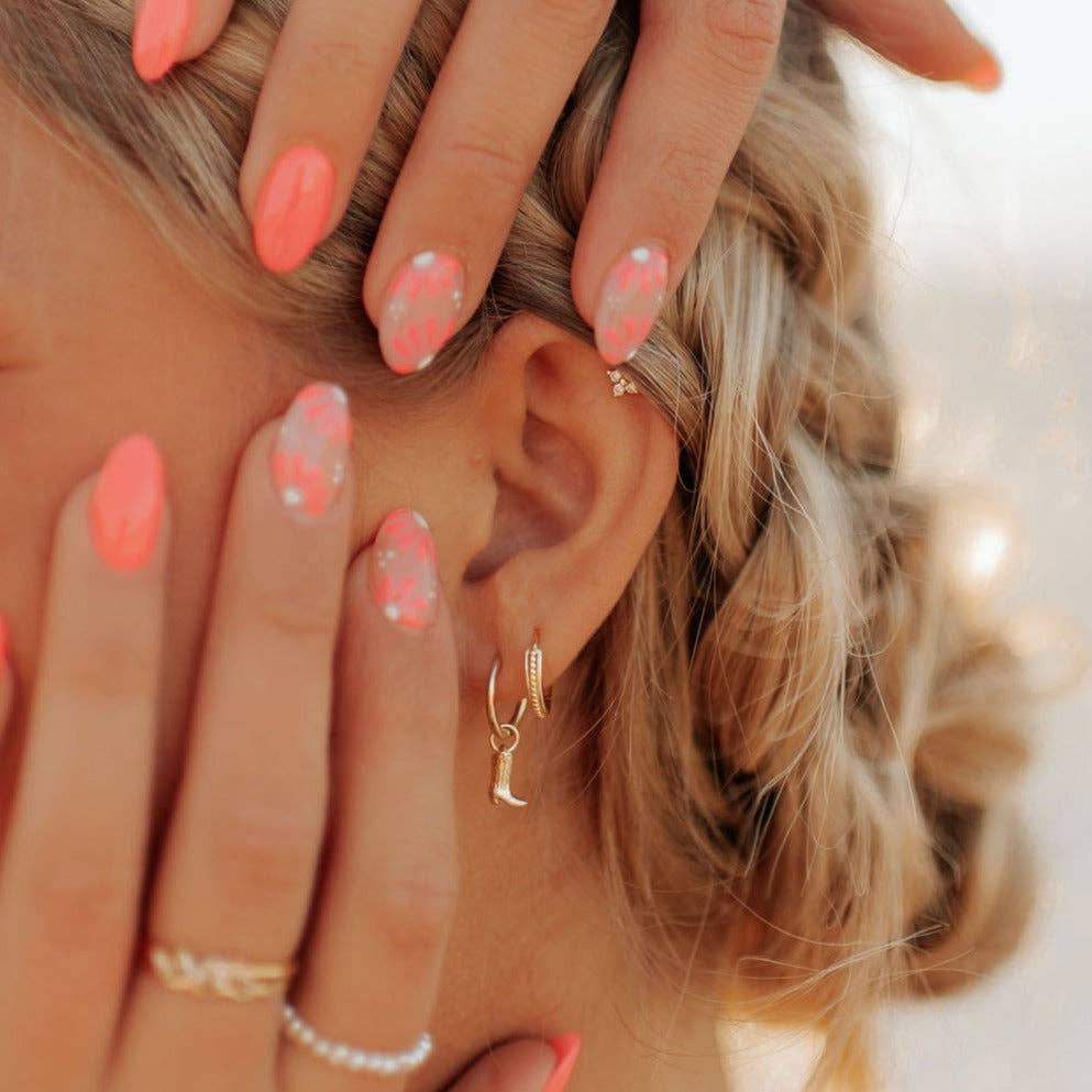 Close-up of a person's hand with pink nail polish touching their hair, wearing gold earrings and rings.