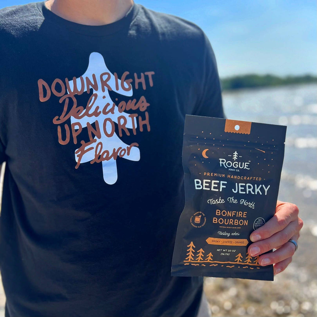Person wearing a black t-shirt with 'Downright Delicious Up North Flavor' text, holding a package of Rogue Beef Jerky.