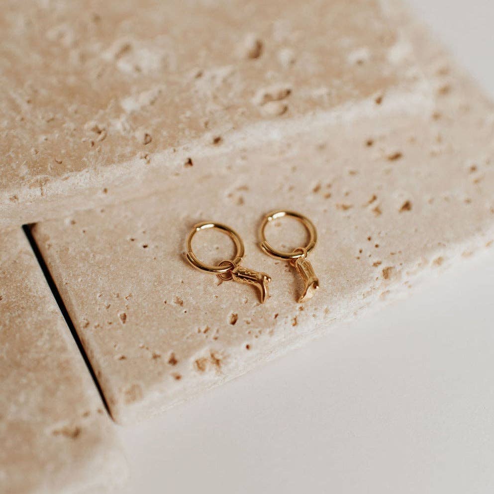 Gold earrings on a textured beige surface