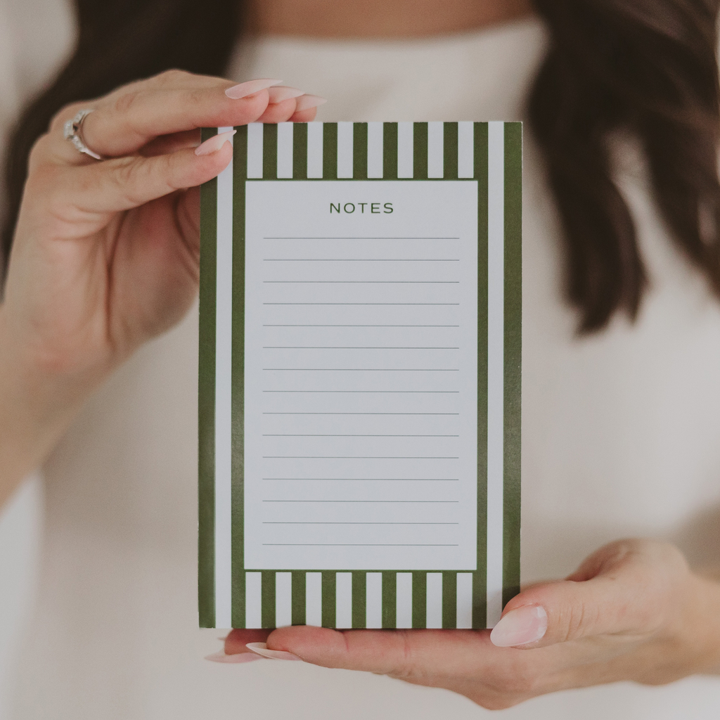 Green and white striped lined notepad with a Notes heading, held upright in two hands.
