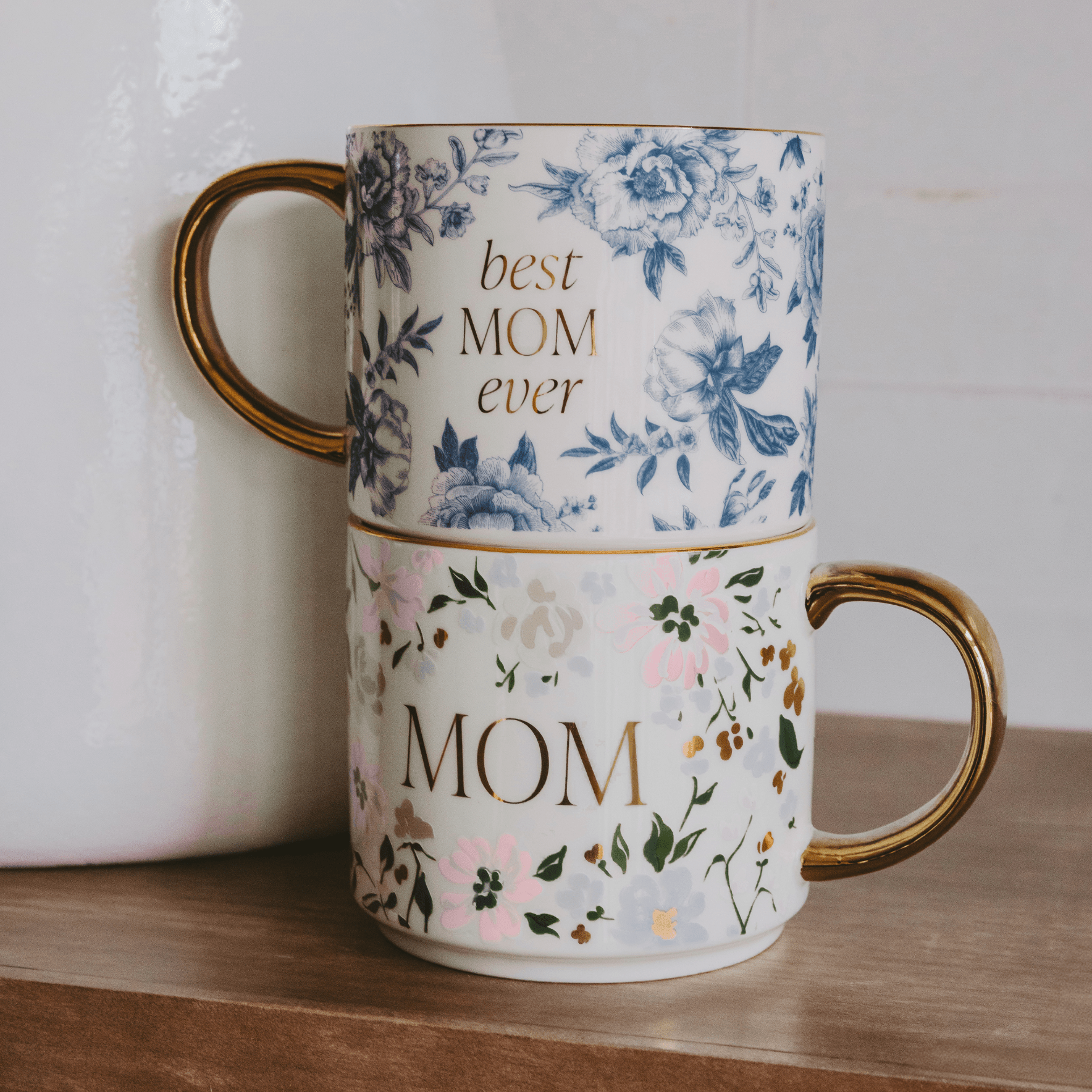 Two floral mugs stacked on a wooden surface with 'best mom ever' and 'mom' text.