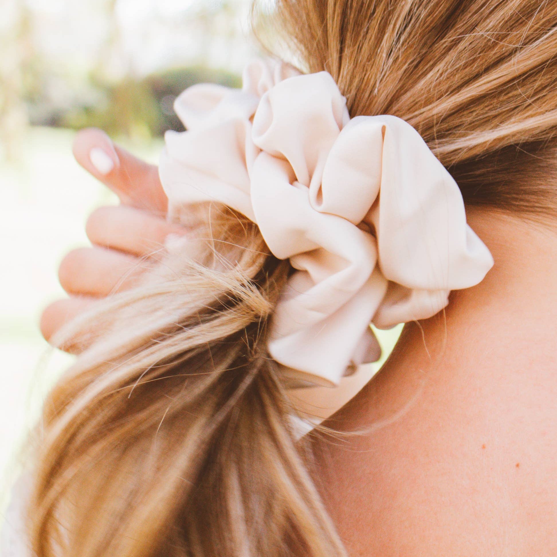 Beige scrunchie in a person's hair with a blurred natural background