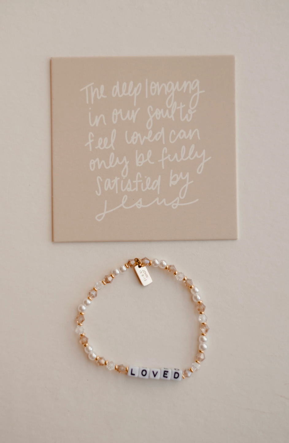 Bracelet with 'LOVED' beads on a beige background with motivational quote